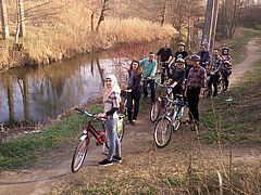 Uczestnicy rowerowego zjazdu w Olsztynie podczas podróży wzdłuż Łyny. Na pierwszym planie grupa rowerzystów, w tle Łyna, wokół las.