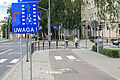 Znak "Uwaga rowerzysta z prawej" - na niebieskim tle ścieżka rowerowa i znak informujący o nakazie udzielenia przerwszeństwa. W tle skrzyżowanie i rowerzysta przejeżdżający przez ulicę